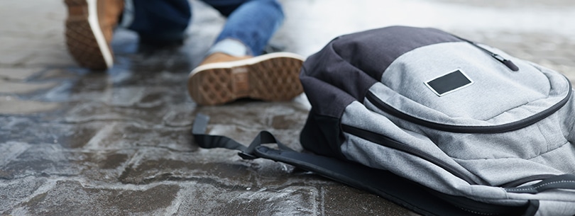 Backpack lying on slippery paving slabs near falling man closeup. Ice injuries concept